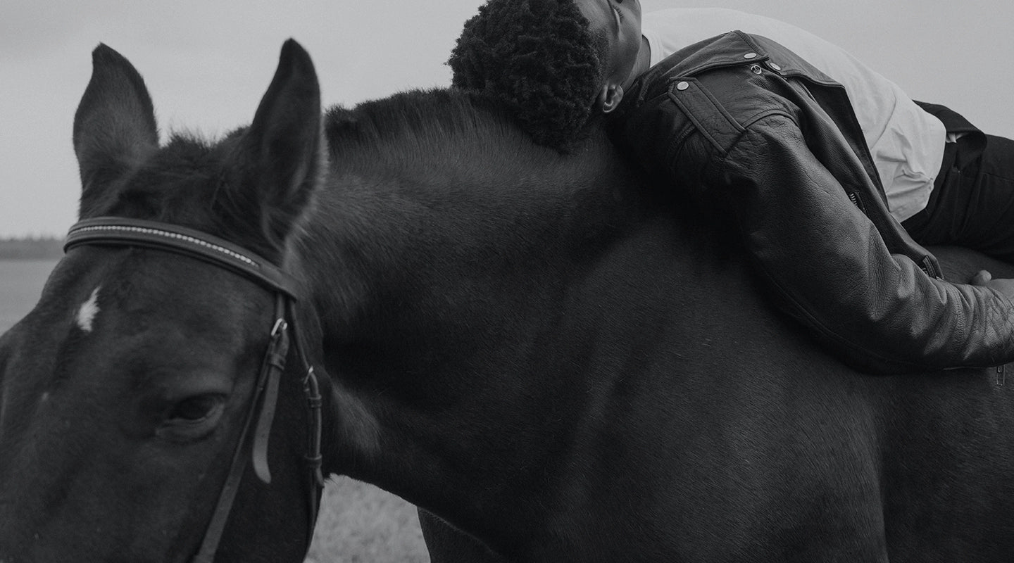 A black and white photograph of a man elegantly sprawled on a horse, reflecting the beauty and depth of contemporary African art photography in this stunning piece.