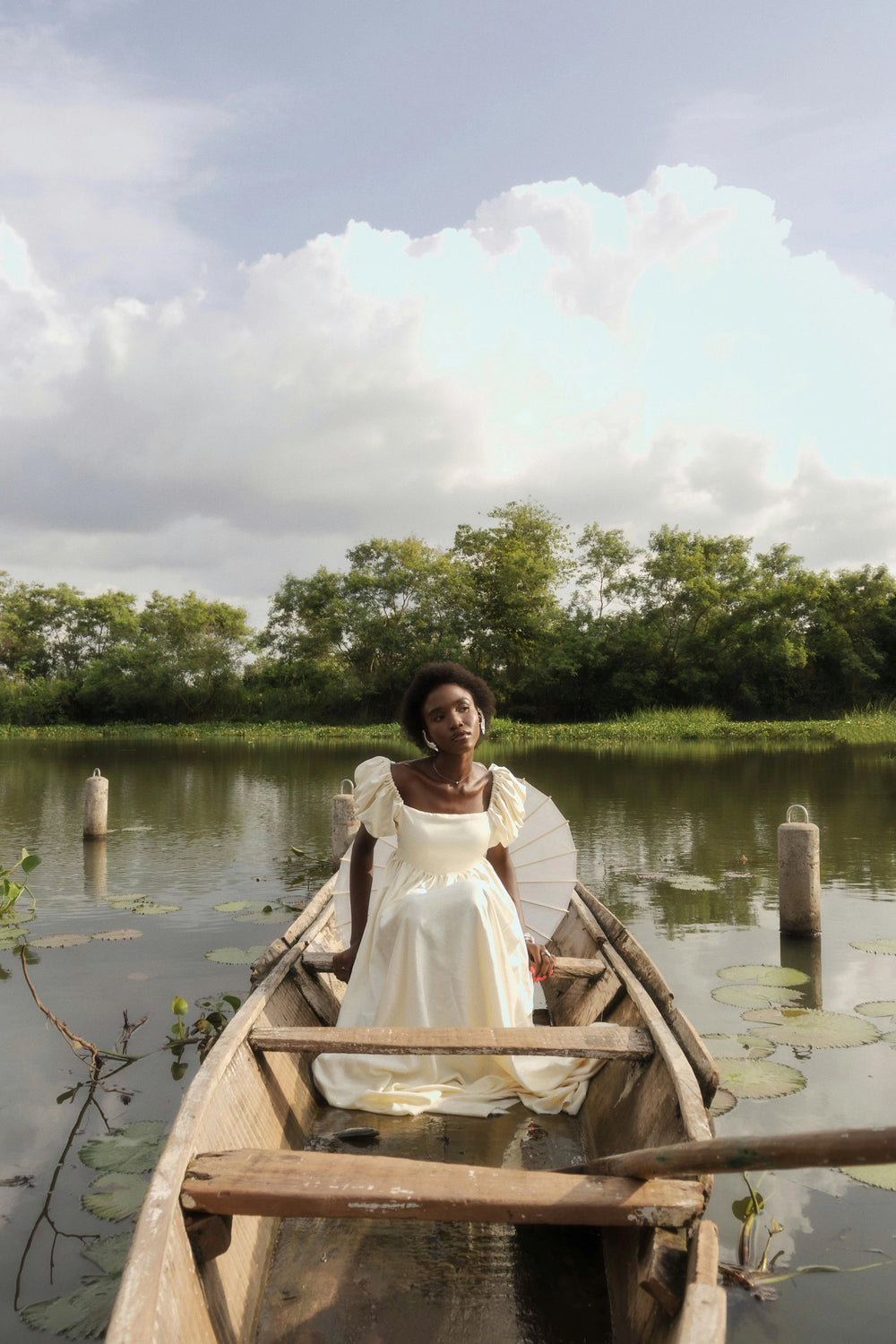 Contemporary African art piece of a woman in a white gown seated in a wooden canoe, blending traditional style with modern expression.