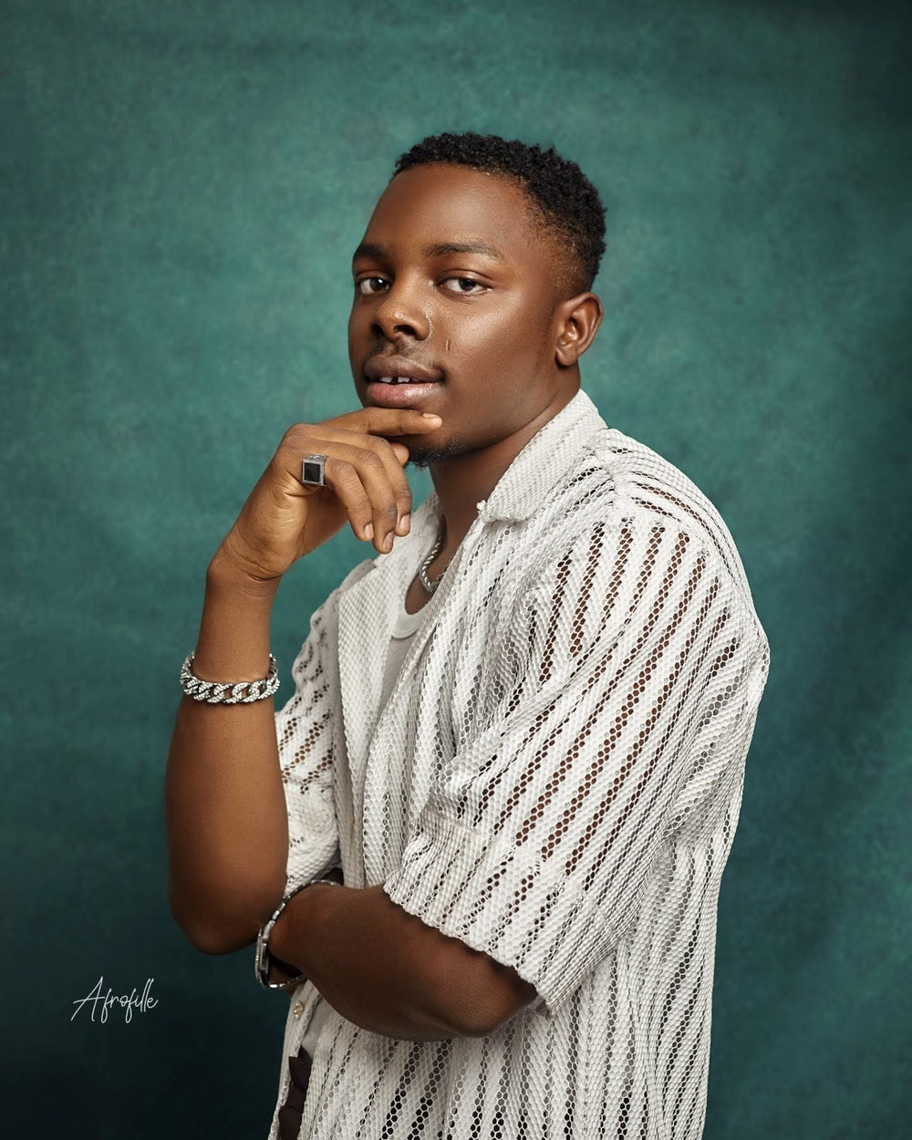 Portrait of Oluwatobiloba Fasalejo wearing a white textured shirt, posing thoughtfully against a teal background